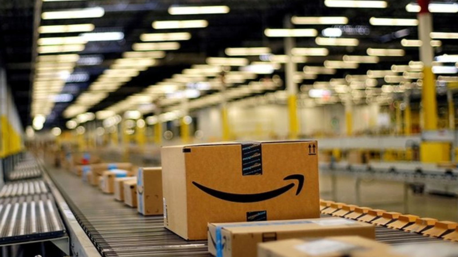 Multiple Amazon packages moving along a conveyor belt inside an Amazon warehouse, illustrating automated logistics and order fulfillment.